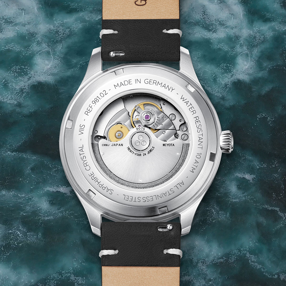 Rückseite der VIIS Flieger GMT 42 „Adriatic“ mit verschraubtem Sichtboden, sichtbarem Miyota 9075 Automatikwerk und fein graviertem Gehäuse aus Edelstahl vor meerblauem Hintergrund.